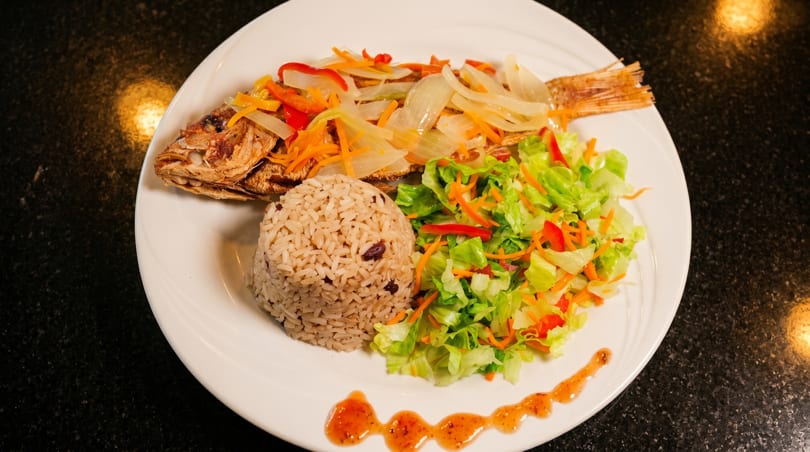 Whole fried fish topped with onions and peppers, served with rice and a side salad.