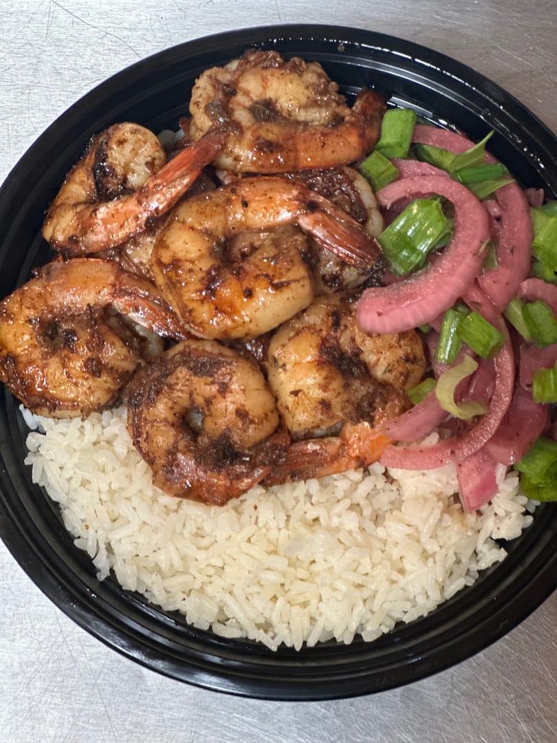 A black bowl filled with white rice, seasoned shrimp, pickled red onions, and green onions.