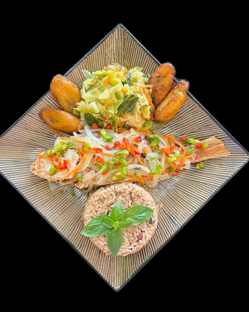 Whole fried fish topped with peppers and onions, served with rice, cabbage, and plantains.