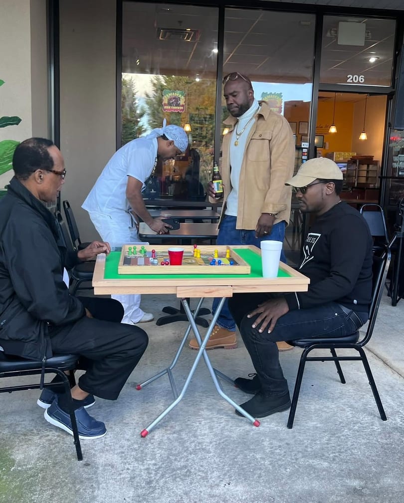 Four men playing a board game on a patio outside a Jamaican restaurant.